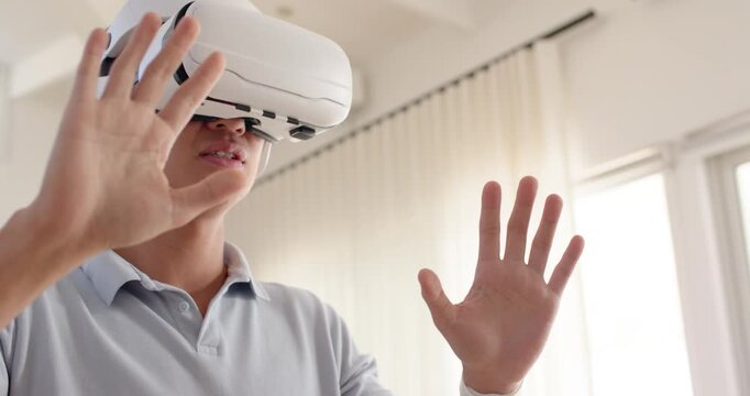 Mid-adult Asian man in polo and smartwatch using VR headset at home exploring and selecting option