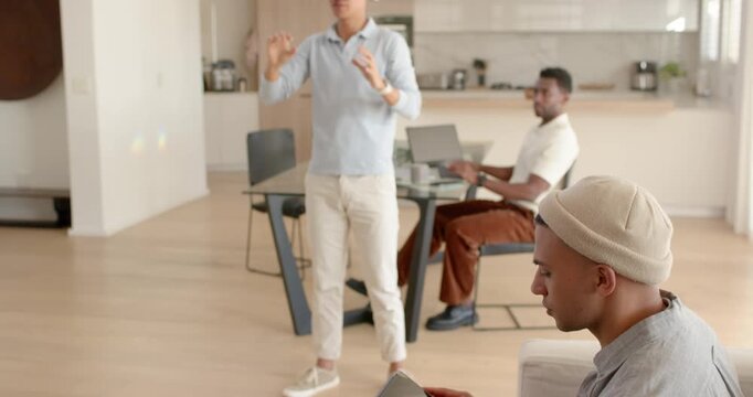 Diverse men watching Asian man donning white VR headset, exploring at home with laptop and tablet