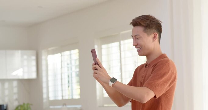 Diverse men in kitchen, beanie holding framed screen, orange polo raising purple phone, reviewing