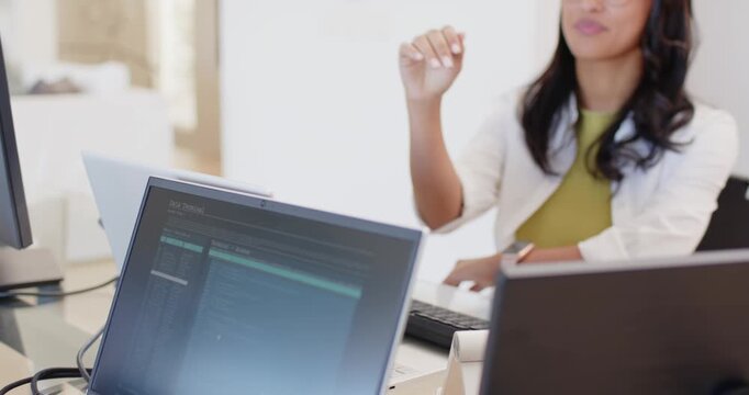 Camera pulling back showing African American woman at office laptop resting chin and smiling at cam