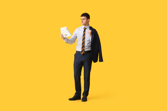 Young man with stylish striped tie and jacket with newspaper on yellow background