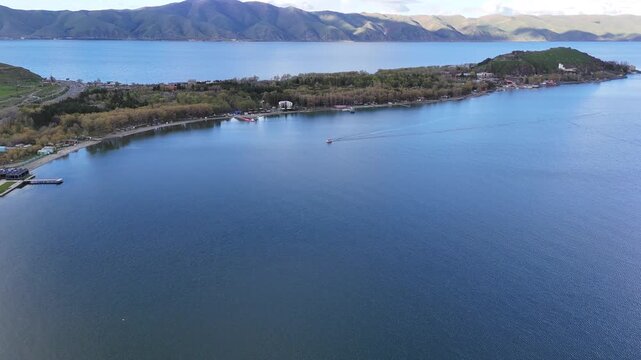 4K Drone Aerial View of Mountain Lake Shoreline With Floating Boat Under Dramatic Cloudy Sky.