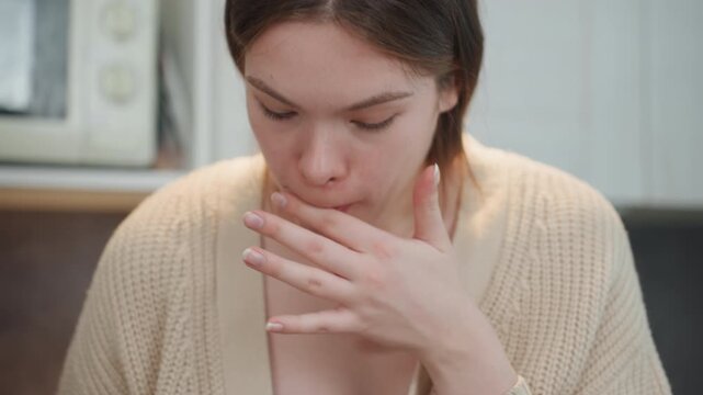 Pregnant woman tasting smoothie in kitchen, closeup of lips and fingers, cardiganclad expectant mother reacting with subtle grimace, touching chest, showing queasy expression and aversion, candid
