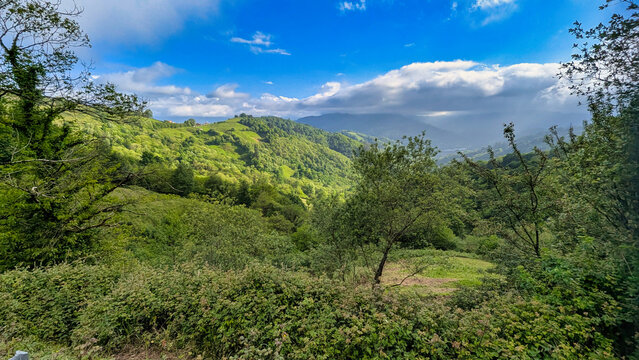 Lush Asturian landscape in La Casilla, between Bimenes and San Mart&iacute;n del Rey Aurelio, with green hills, dense forests, scattered houses, and dramatic cloud-filled sky, Asturias, Spain