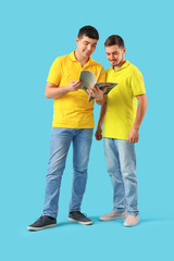 Fototapeta premium Handsome young brothers with magazine on blue background