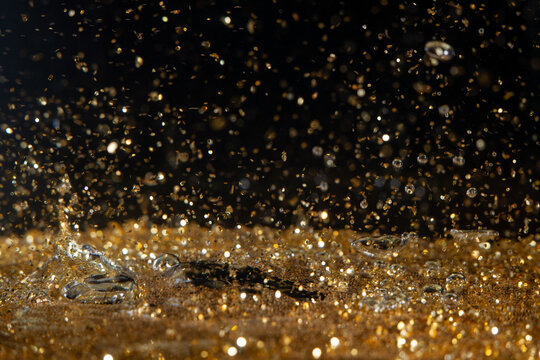 Water droplets create splashes in golden liquid with bright reflections during daytime
