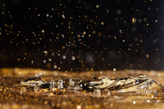 Water droplets create splashes in golden liquid with bright reflections during daytime