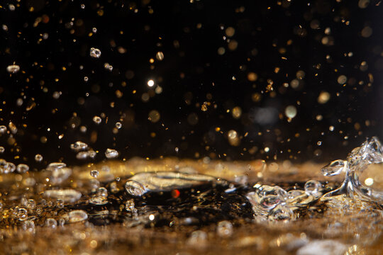 Water droplets create splashes in golden liquid with bright reflections during daytime