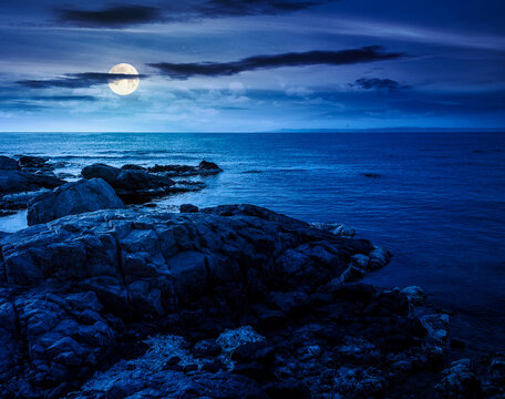 sea coast with stones and rocks at night. summer vacation background. full moon over seascape with rough terrain. fantasy relaxing at the sea. mysterious coast of bulgaria