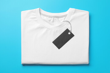 Naklejka premium Blank folded t-shirt with tag on light blue background, top view. Mockup for design