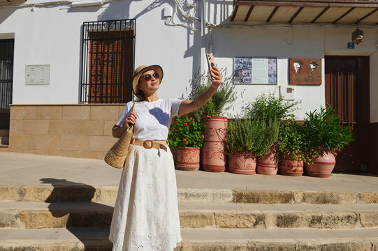 Peal de Becerro, Andalusia, Spain - 28th May 2026:  Woman travelling in a small Spanish village taking a selfie in summer with hat and straw bag