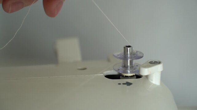 Close-up of beige thread winding onto an empty sewing machine bobbin from a stationary spool during thread preparation.
