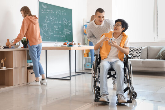 Teenage boy with his classmate in wheelchair using mobile phone at school
