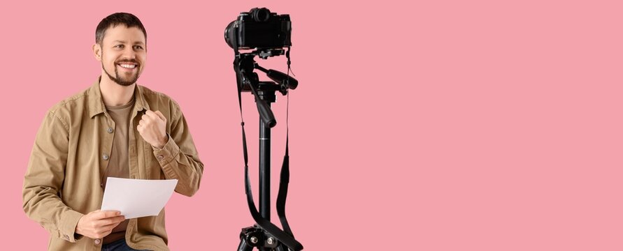 Male actor with movie script recording video on pink background with space for text