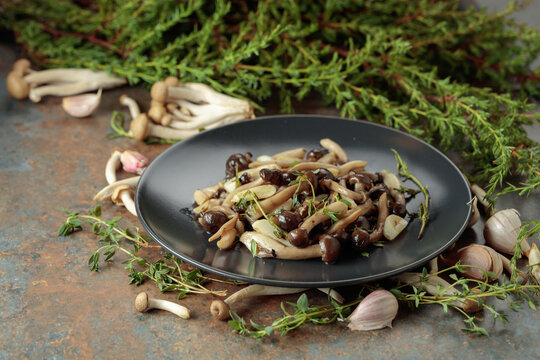 Fried shimeji mushrooms with thyme and garlic on a black plate.