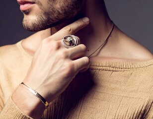 Fototapeta premium Close-up of a man in tan clothing, adorned with a ring and bracelet, touching his neck, with a necklace