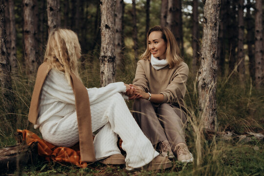 Two women sitting in forest holding hands symbolizing female emotional safety forest therapy healing conversations and nervous system co regulation