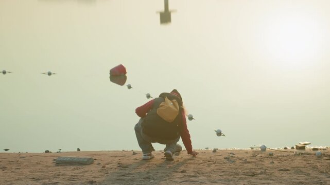 Backpack silhouette at sunset shore, kneeling to skip stones along quiet waterline, golden haze backlighting figure, reflective mood, lone traveler ritual, gentle ripples and scattered pebbles