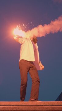 A young person stands on stone steps against a twilight sky, holding a flaming torch aloft, evoking rebellious energy and a carefree spirit.