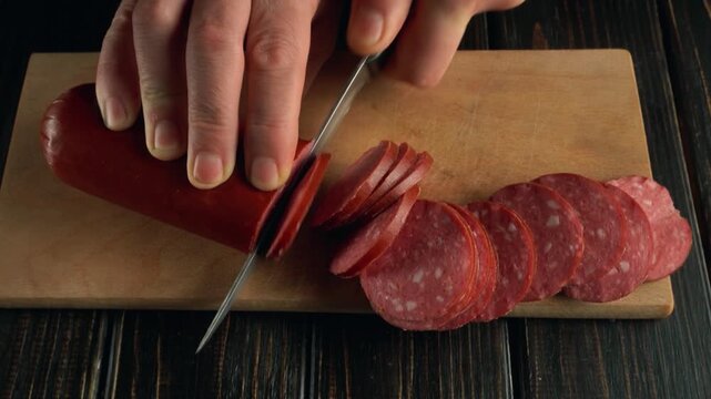 Hands slicing sausage into thin rounds on a wooden cutting board, showcasing the progression of the cutting action in a kitchen setting