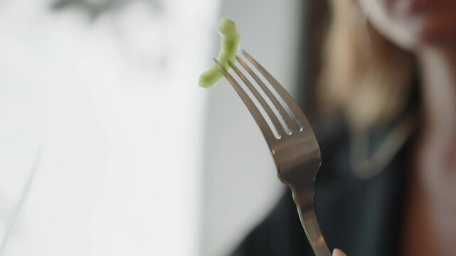 Closeup fork balancing cucumber slice, white woman mindful eater hesitating near window muted tones, soft overcast light, reflective mood, slow tasting and thoughtful pause during diet test.