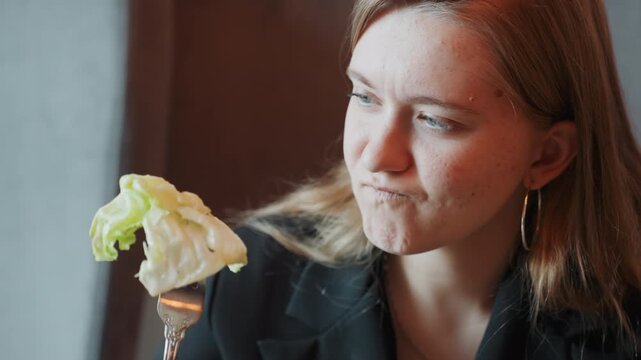White woman inspects lettuce with skepticism. Professional food critic scene in bistro, focused palate testing and analytic gaze, crisp but wilted leaf on fork, furrowed brow and tasting hesitation,