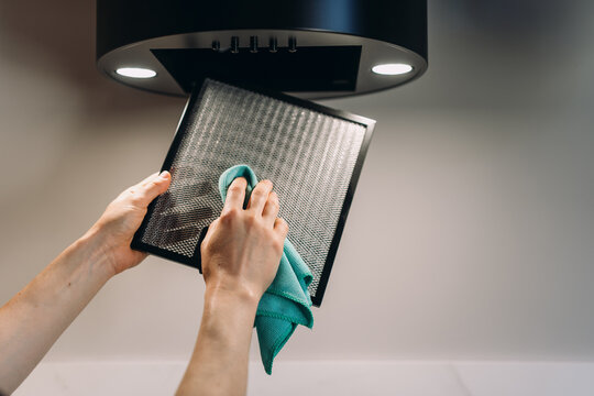 Woman cleaning dirty removable filter from kitchen extractor hood
