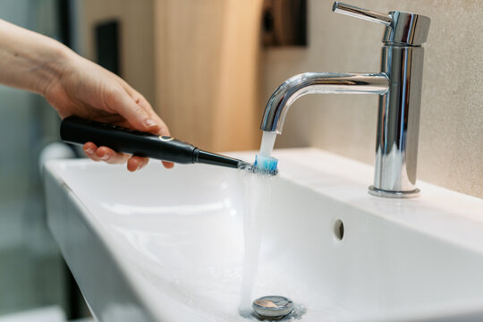 Woman washing electric toothbrush in modern bathroom sink