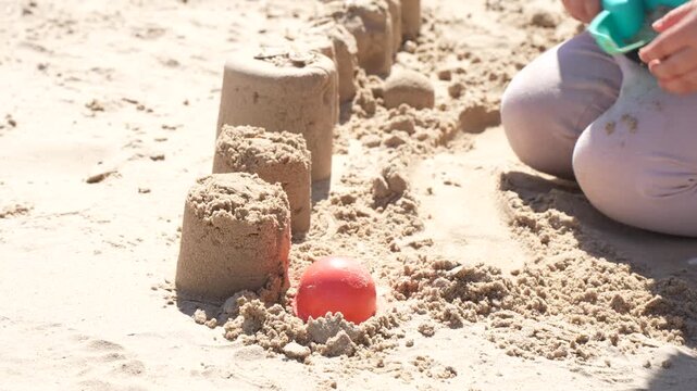 Toddler hand lifting a red plastic mold from a fresh sandcastle row on the beach, sensory play and early childhood development business concept