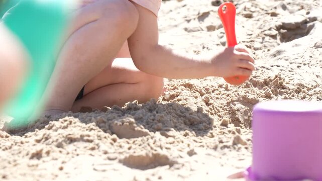 Little toddler crouching in sandbox and digging mounds with colorful plastic toys representing early childhood education backyard leisure and sensory activities