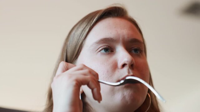 Closeup young woman tasting salad in slow mindful bites, hoop earrings and freckles visible, camera focuses on lips and fork, expressive facial reactions, soft natural light, intimate dining closeup