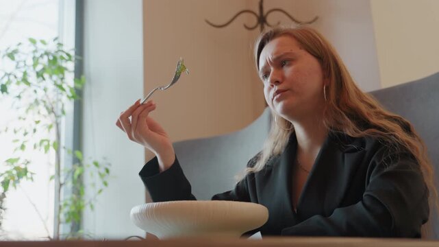 Caucasian woman hesitating over salad by window, student role studies forkful against plant backdrop, soft daylight, reflective expression, subtle head tilt, modern cafe interior, decision moment,