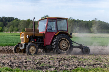 Obraz premium Person carrying a large white sack while walking on an agricultural field with plowed soil ridges during spring seasonal farming work in the countryside