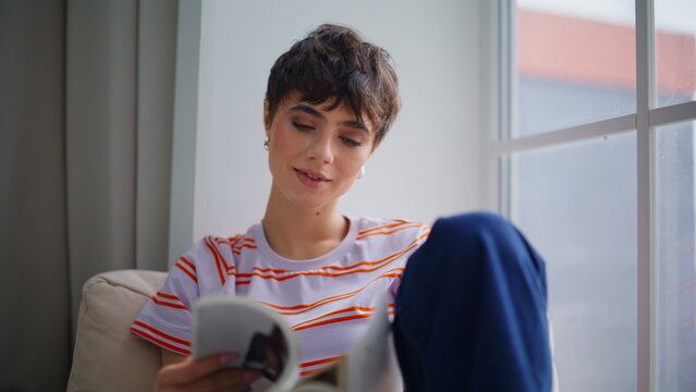 Smiling woman reader engaged with magazine in calm home environment closeup.