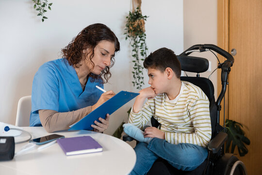 Nurse writing during home visit with boy in wheelchair