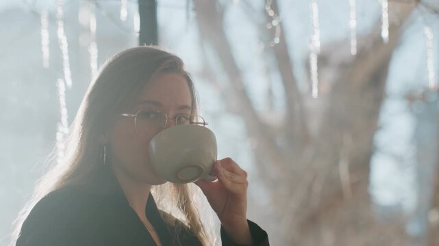 White woman contemplative portrait by window with icicles, holding cup and gazing thoughtfully, rimlight highlights hair and glasses, serene creative atmosphere, soft winter backdrop and gentle