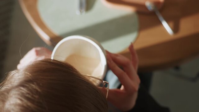Ceramic cup held gently. Closeup of hands holding warm drink. Intimate scene of woman enjoying breakfast quietly. Serene moment of woman sipping coffee on wooden table in morning light