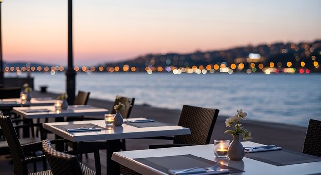 Empty waterfront restaurant tables set for dinner with city lights reflecting on the water at dusk