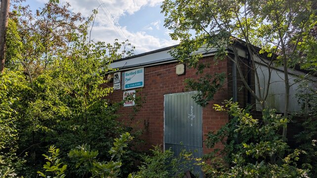 Derelict former Hartford Hill Pool Northwich 21.06.25 Boarded up sealed brick building hidden entrance. Overgrown dense foliage taking over, nature reclaiming. Public abandoned swimming baths site.