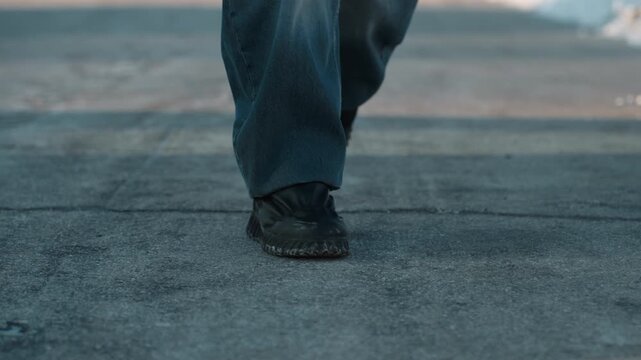 Closeup feet walking on cracked rooftop pavement, worn boots and denim, slow deliberate steps, textured concrete fissures, soft dusk light, long shadow, lonely resilient mood, weathered tread leaving