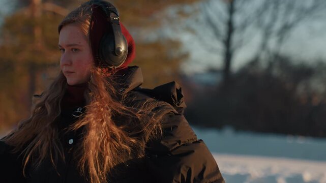 Closeup winter portrait of headphone listener with red gloves and hooded parka, expressive eyes and contemplative gesture in golden cold light, intimate emotional tone and candid sincerity