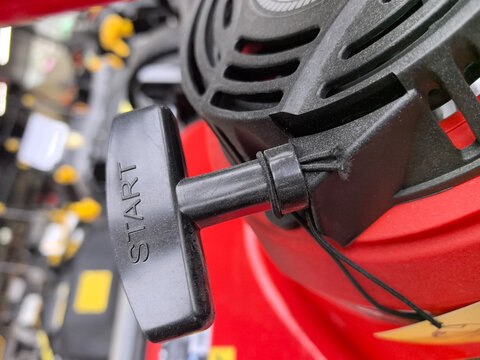 A bright red lawnmower with a shiny pull-start mechanism sits ready for action