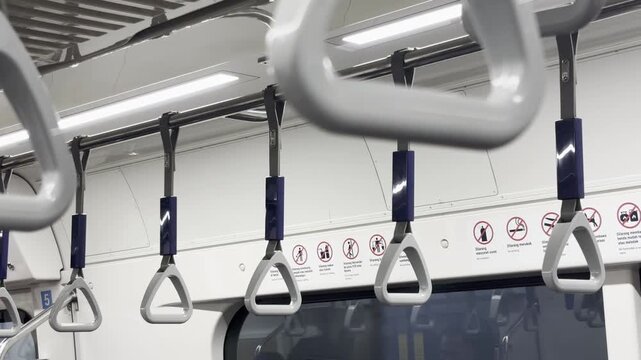 Close-up tracking shot showing a neat row of clean, white triangle plastic hand straps hanging from a metal rail inside a brightly lit modern train carriage.