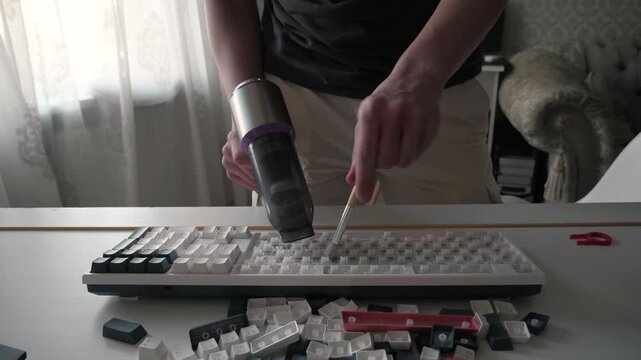 Hands cleaning keyboard, close up of hands removing white keycaps, scattered caps and tools on table, daylight through curtain, focused hobbyist performing precise