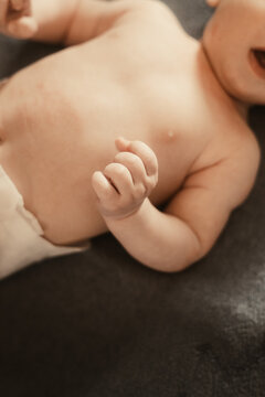 Close-up of a baby lying on a dark grey blanket, showing the chest, torso and a small hand.