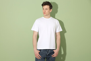 Fototapeta premium Handsome young man wearing blank white t-shirt on light green background. Mockup for design