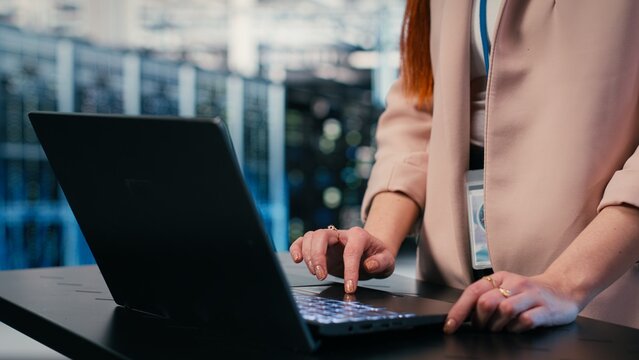 Close up of engineer typing on laptop in server farm, doing network management virtualization, Data center admin overseeing large scale IT infrastructure supercomputers with notebook, camera B.