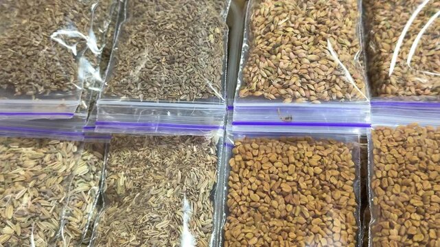Different aromatic spices such as coriander cumin and assorted seasonings packed in small transparent bags with colorful natural textures for cooking use.