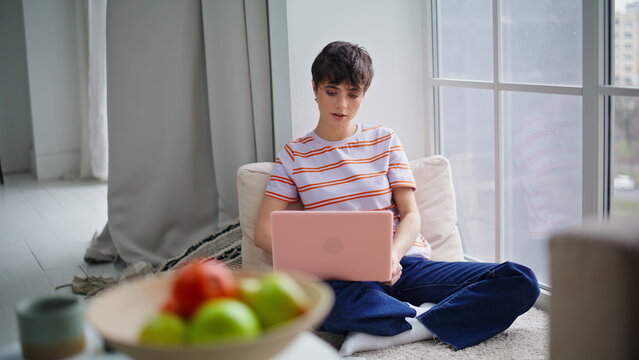 Remote worker using laptop sitting floor modern home. Woman reviewing emails
