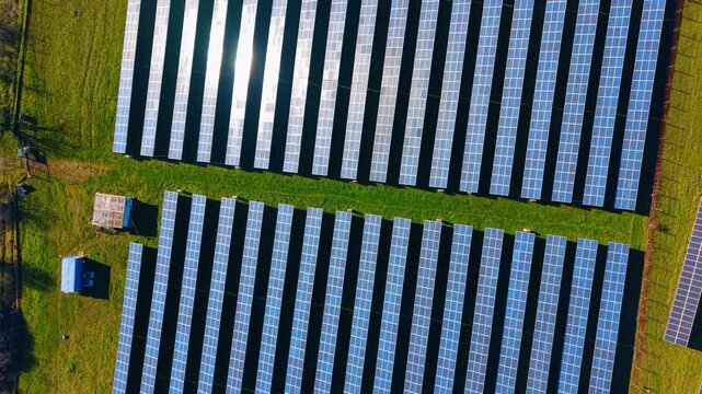 Solar panels top down aerial view. Overhead drone perspective of parallel photovoltaic solar panel rows on a green grass field with sun reflection.